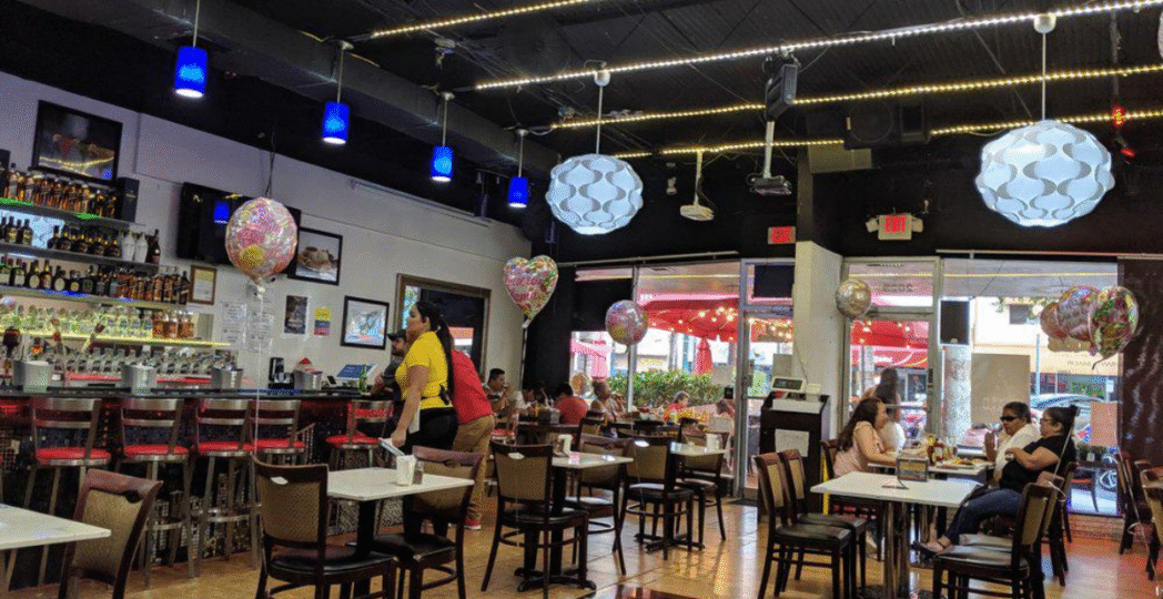 Interior of a vibrant Colombian restaurant with colorful balloons, a bar with liquor bottles, and guests enjoying meals at tables.