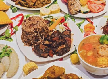 A vibrant spread of traditional Jamaican food featuring rice and peas, oxtail stew, chicken soup, and patties with vegetables and corn.