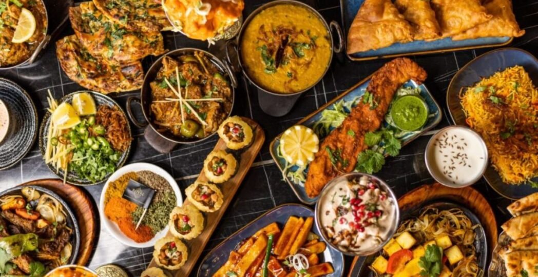 A vibrant spread of traditional Pakistani food including biryani, samosas, curries, naan, kebabs, and chutneys served on a festive table.