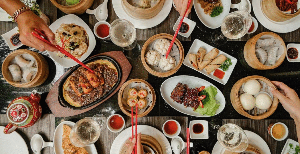Traditional Chinese food table with dumplings, spring rolls, noodles, and steamed buns.