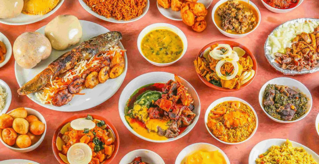 Traditional Nigerian food spread with assorted dishes including jollof rice, grilled fish, fried plantains, soups, and stews.